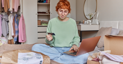 Student zit op haar kamer met allerlei pakketjes om haar heen en heeft een bankpas in haar hand en checkt haar saldo op haar latop